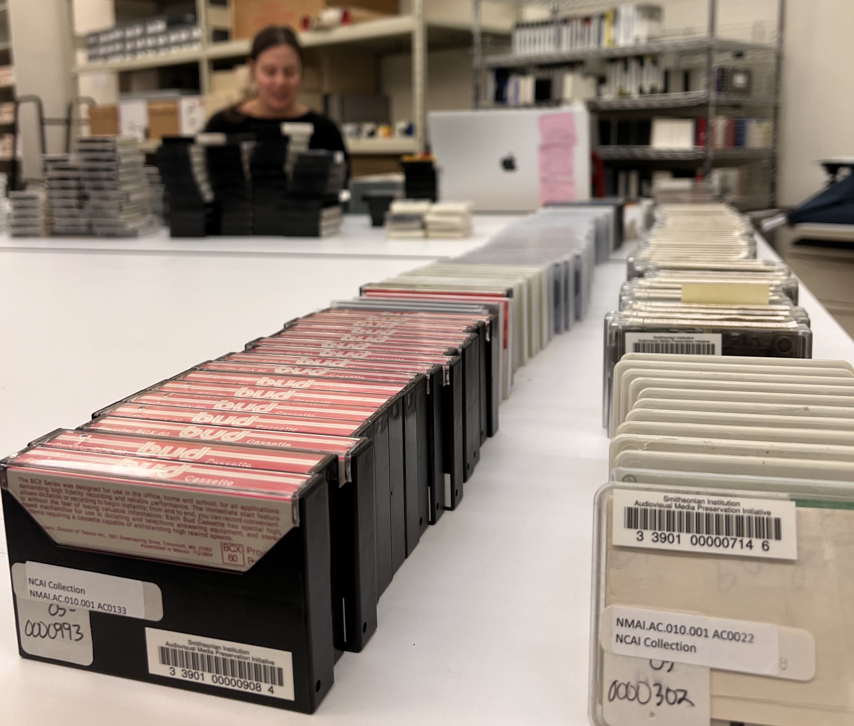 Orderly line of audio cassettes receive barcodes on table.