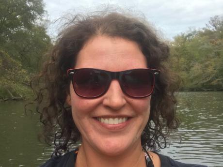 Crystal Sanchez wearing sunglasses with a lake and trees in the background.